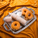 Load image into Gallery viewer, Two donuts and a skincare product on a decorative tray with an orange fabric background
