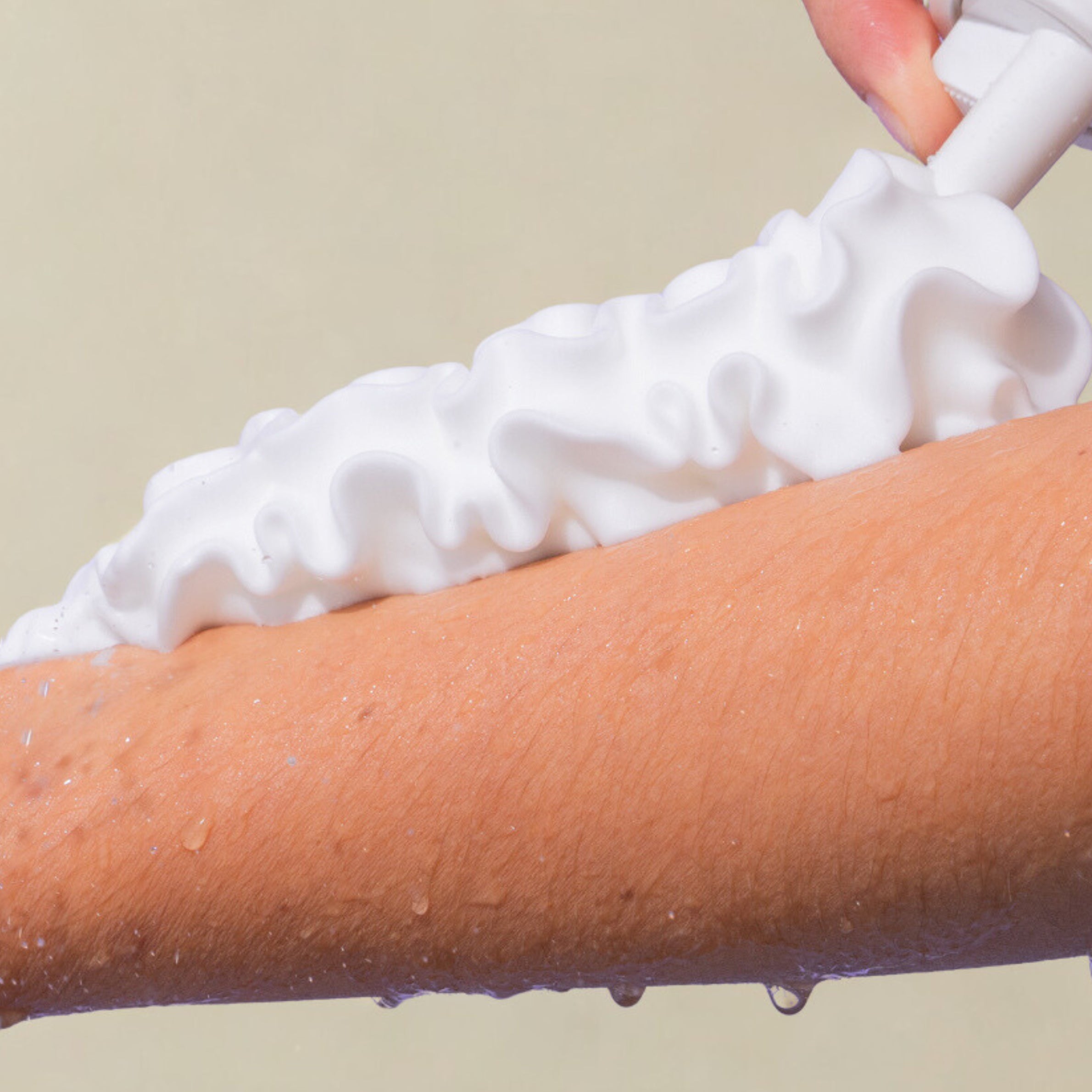 Person applying white foam to a arm against a beige background